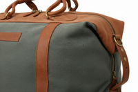 Side view close-up showing canvas texture, leather trim, stitching and brass hardware detail